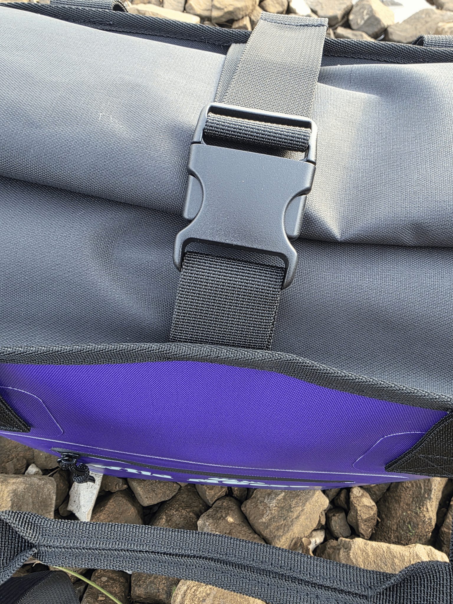 Purple tote bag with a buckle over the top on a rocky beach