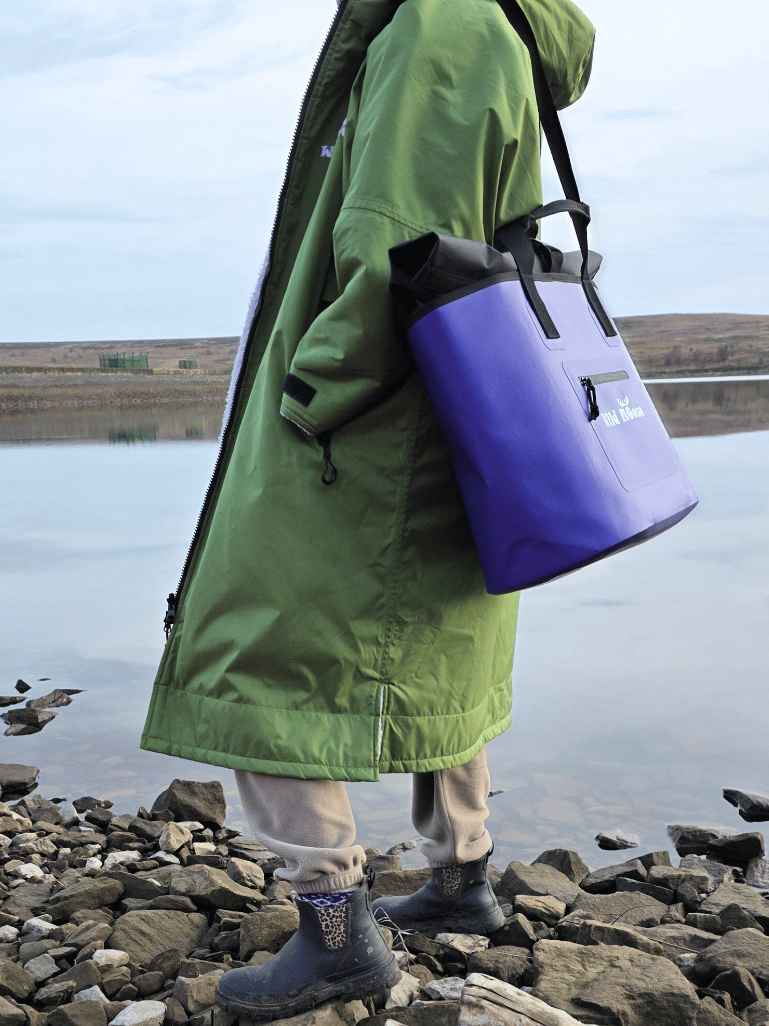 lady with purple tote bag over shoulder wearing a green robe looking at a rocky lake
