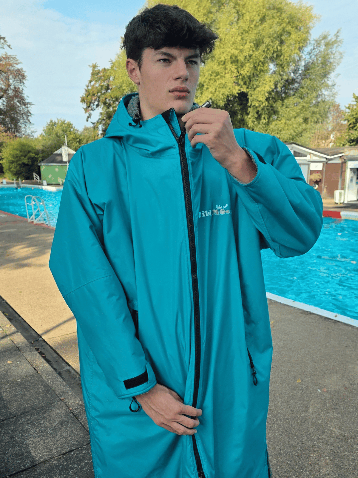 man in green changing robe doing up zip. Stood next to a lido