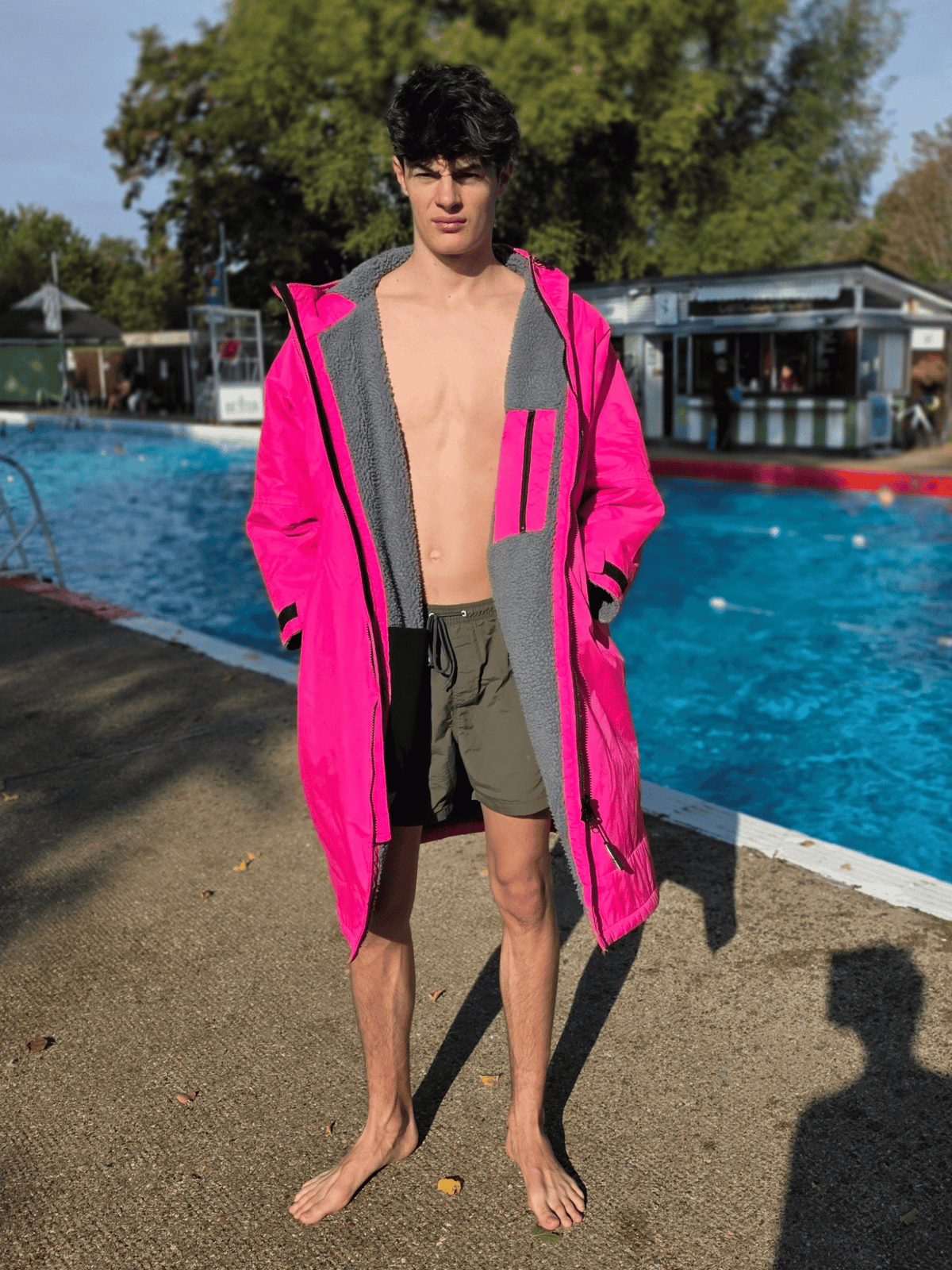 man in swim shorts and bright pink changing robe stood next to a lido on a sunny day
